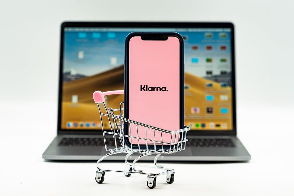a smartphone in a small shopping cart in front of a macbook