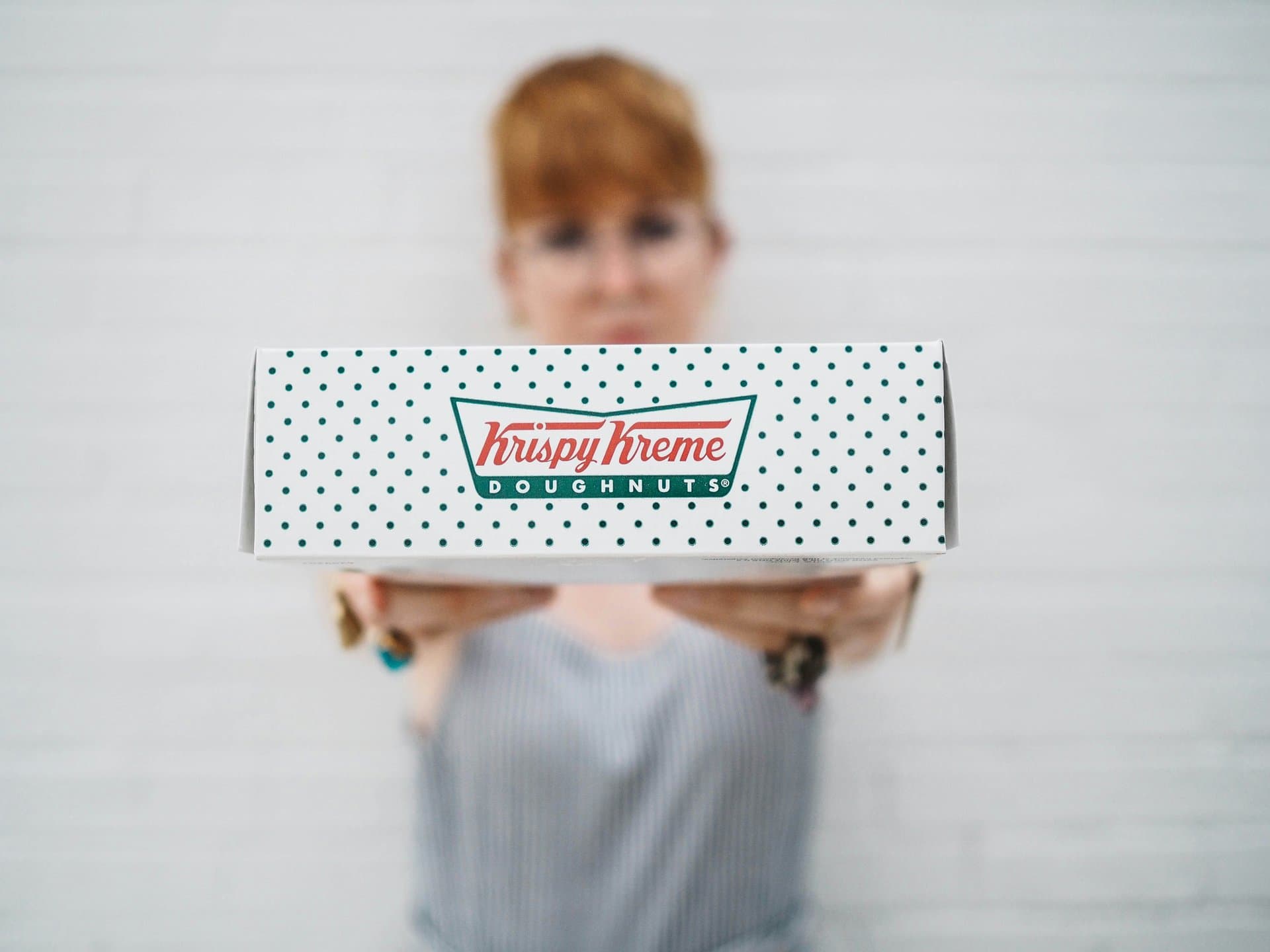 a woman holding a box with Krispy Kreme written on it